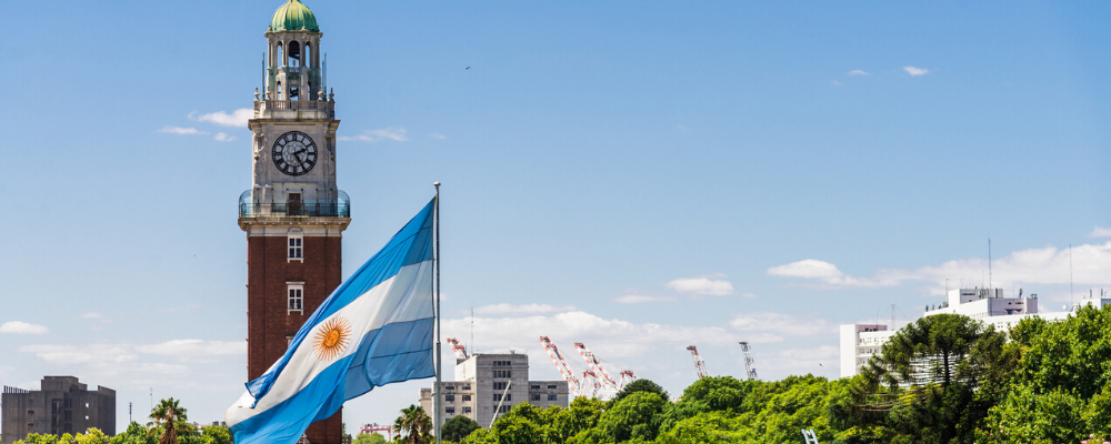 The Torre Monumental clock tower in Buenos Aires, Argentina, rising behind a large, waving national flag.