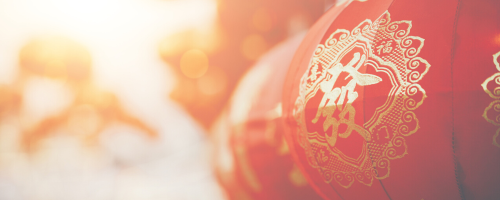 Close-up of festive red Chinese lanterns with gold calligraphy and designs against a warm, blurred background.