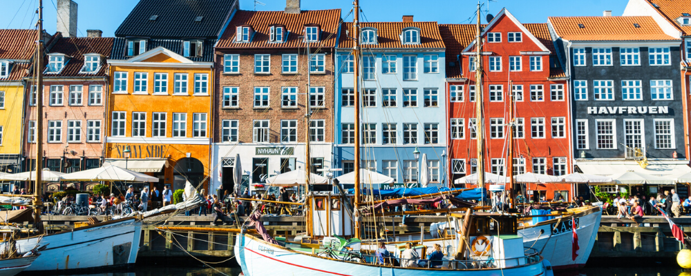 Colorful waterfront row houses lining a canal with docked sailboats in Denmark.