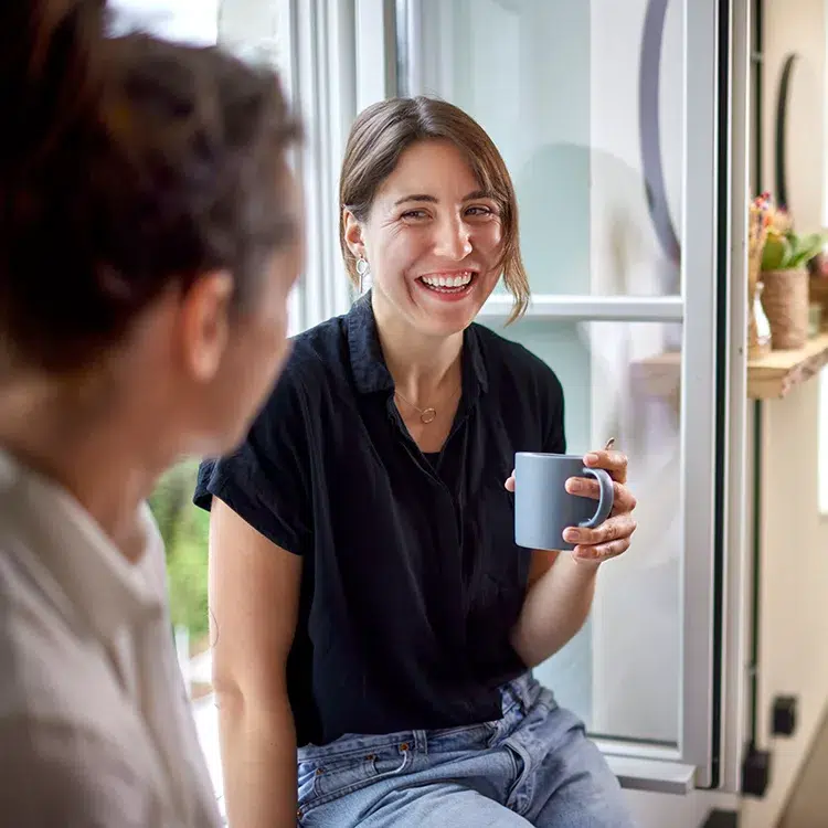 woman holding a mug and smiling at woman across from her