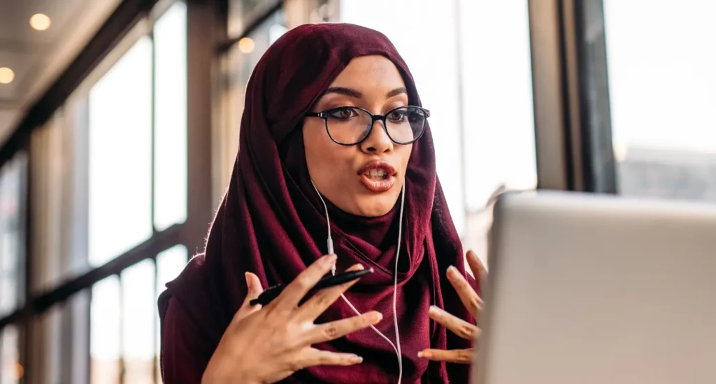 Woman teaching a class on laptop, wearing a headscarf and earpods
