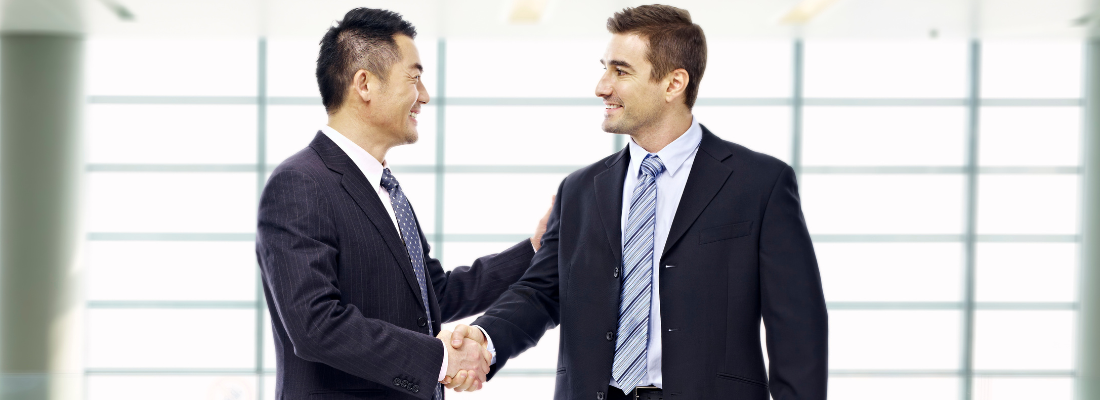 two business professionals shaking hands and smiling in an office setting