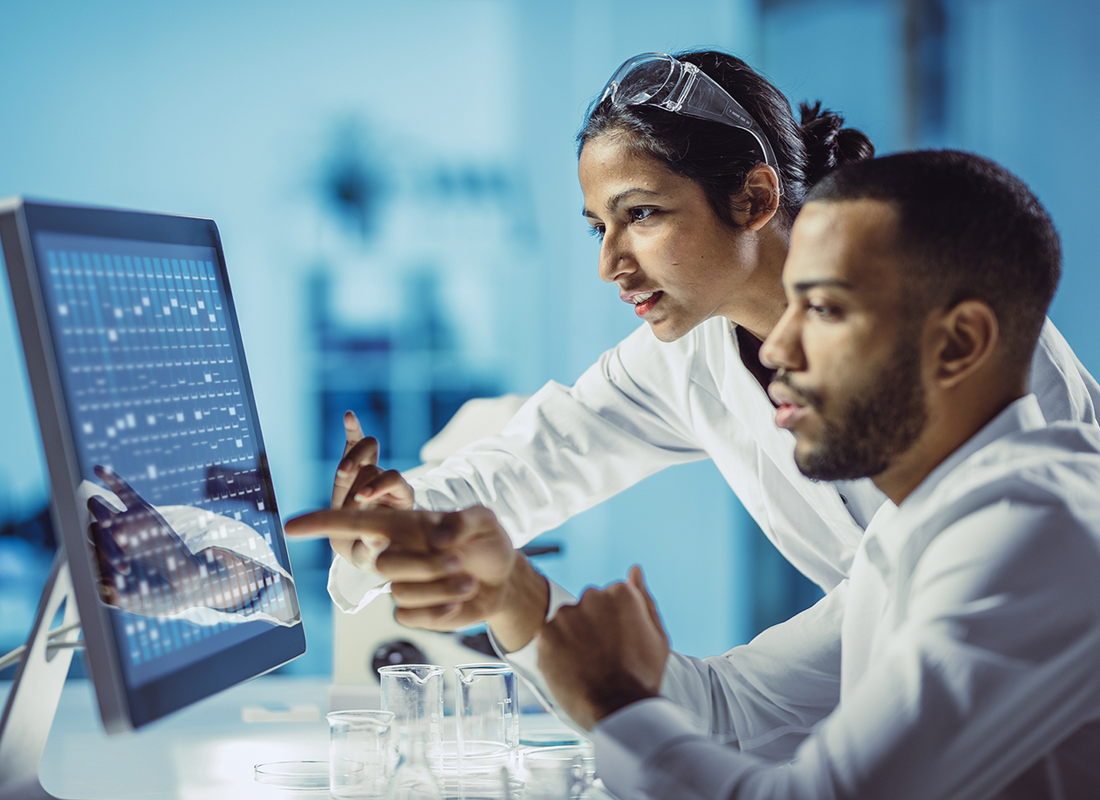 Image of two life sciences employees in lab coats studying data on a computer