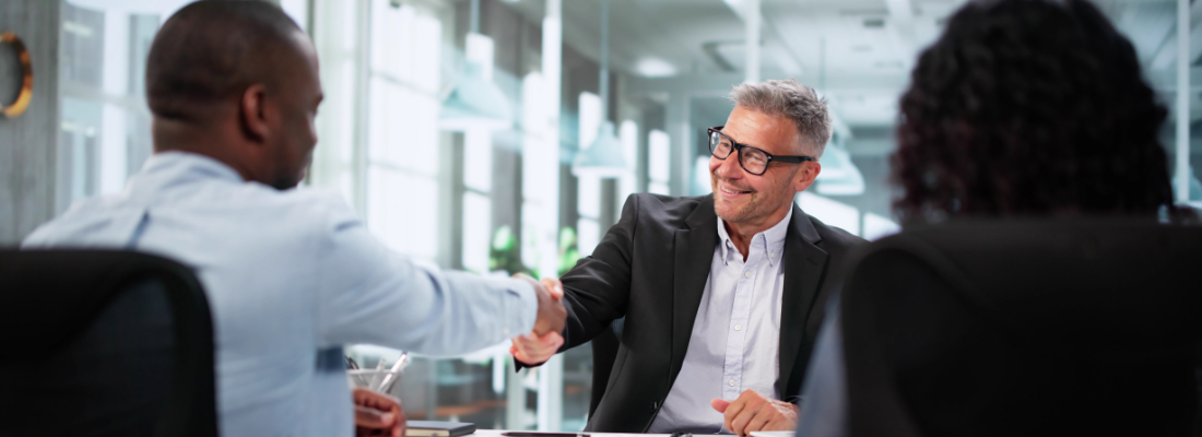 two professionals shaking hands at a table in an office