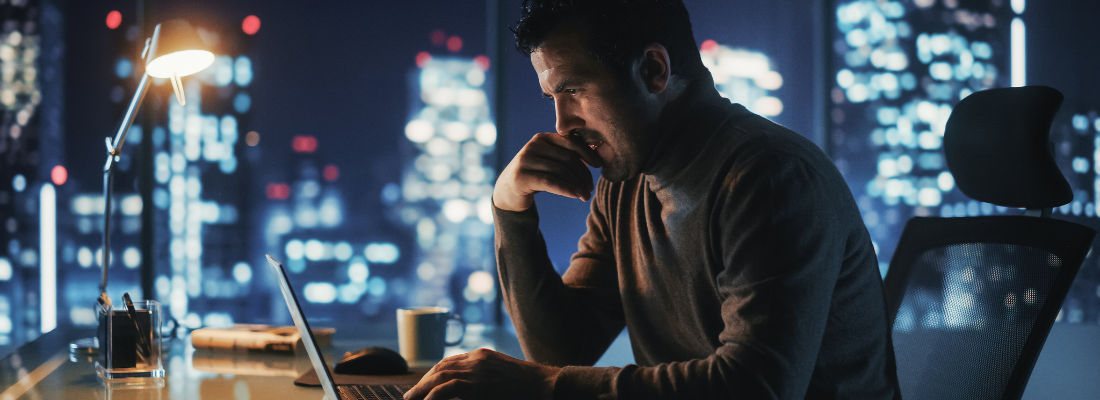 a man looking at a laptop screen in an city business setting at night